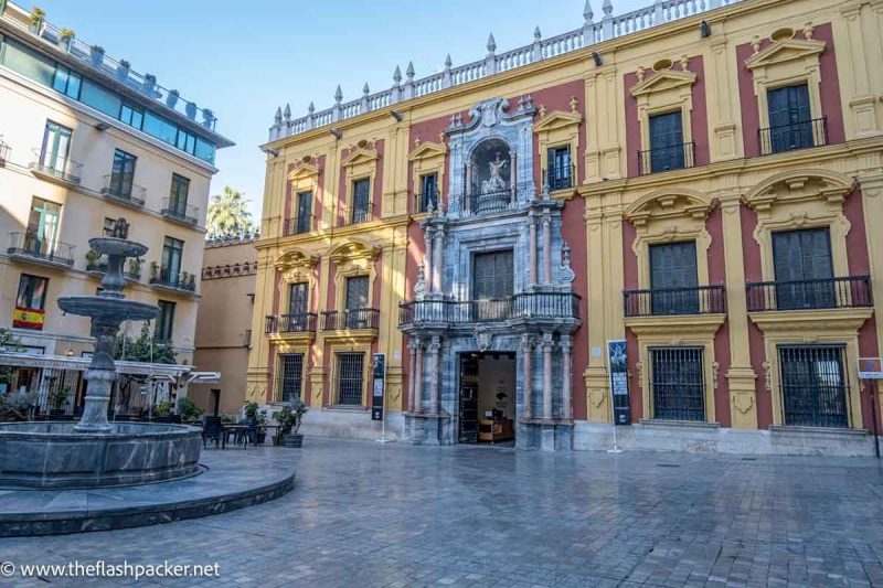 red and ochre and marble facade of baroque building in square with central fountain