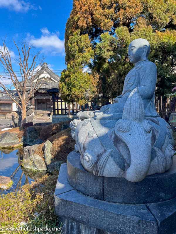 large stone statue in front of a pond and small temple