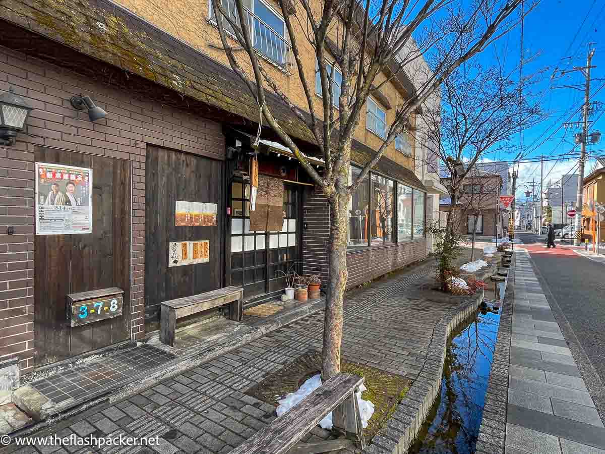 2 storey wood and brick buildings on a street lined with a small canal