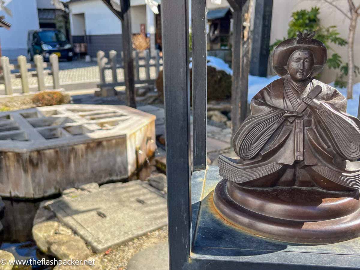 small bronze sculpture of a japanese figure next to a geometric shaped well cover