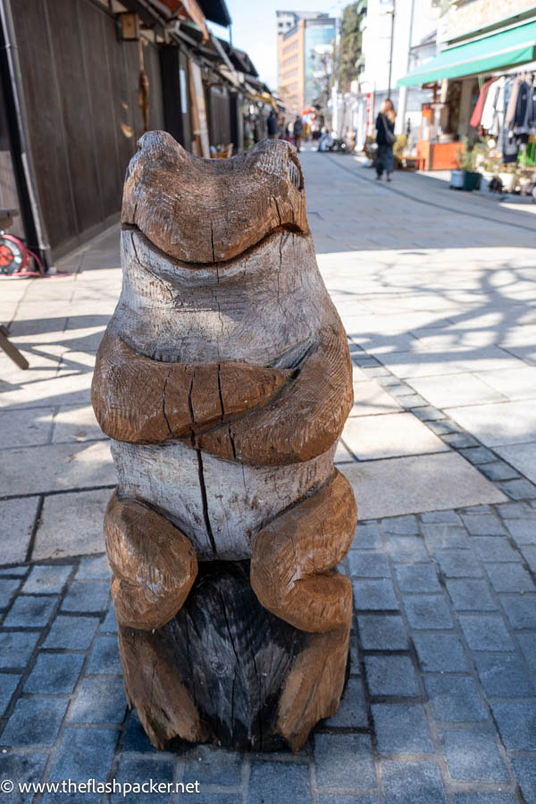 wooden sculpture of a frog with folded arms