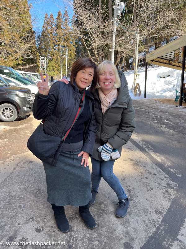 two women posing for a photo in a snow covered car park