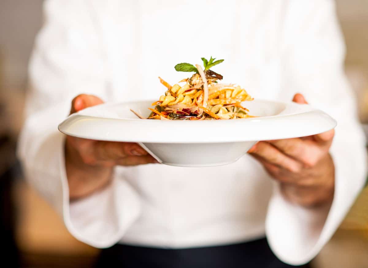 chef holding pasta meal in a white bowl