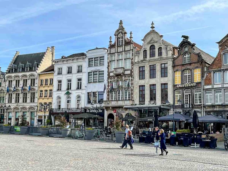 people walking past cafes in front of gabled medieval buildings