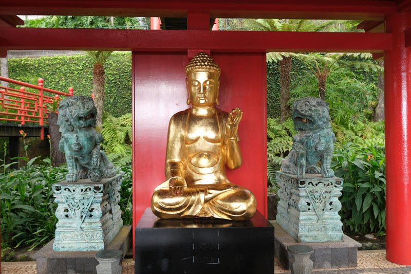 bronze buddha flanked by two stone lions at monte palace tropical garden madeira