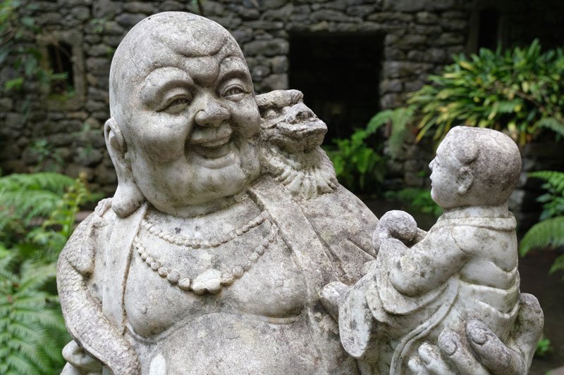 a stone laughing buddha holding a small child in his palm