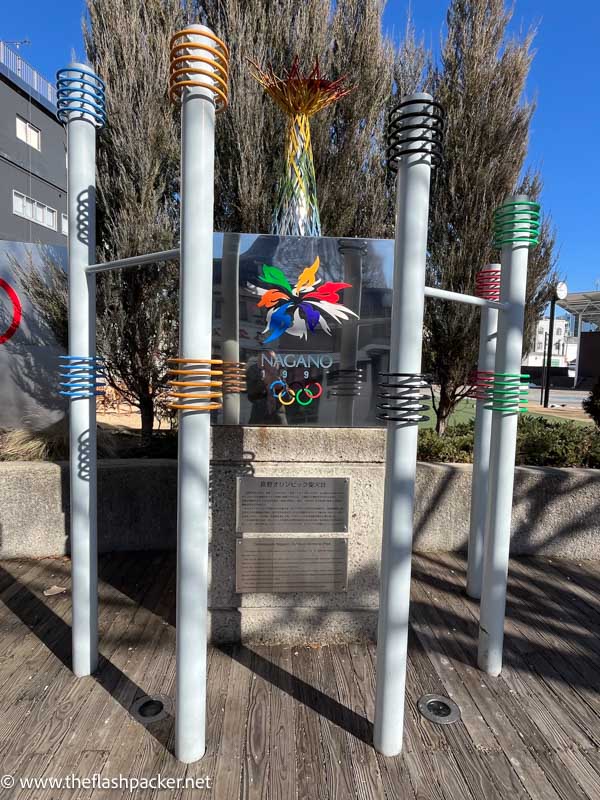 monument to nagano olympic games with plaque and poles with coloured rings