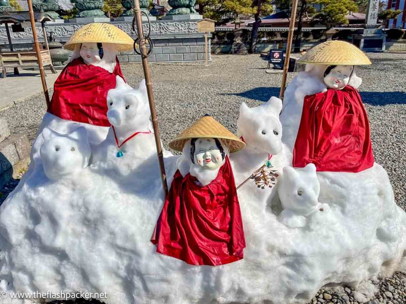 small smiling buddha statues in the snow with snow creatures