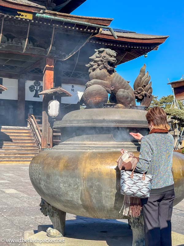 woman holding her hand out at large incense burner in front of a temple in japan