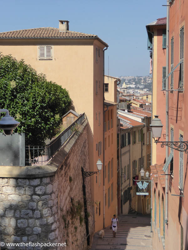 woman walking up steps with dog between ochre colored buildings