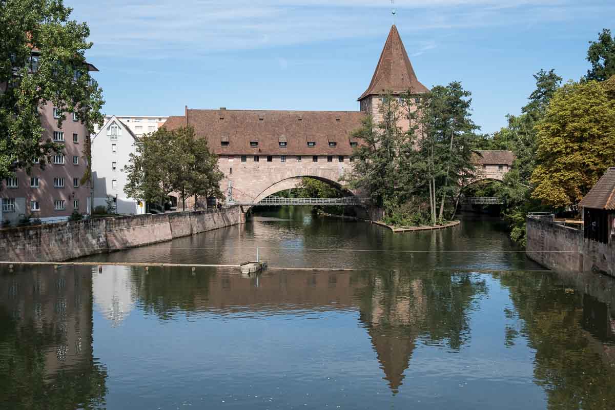 old covered chain bridge with small tower over river with reflections