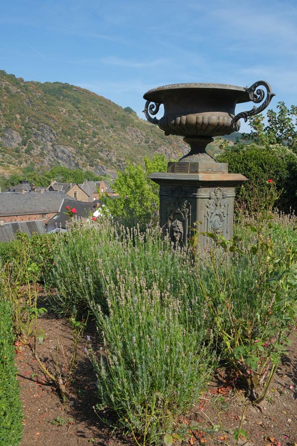 statue of an urn in a garden with hillside in background