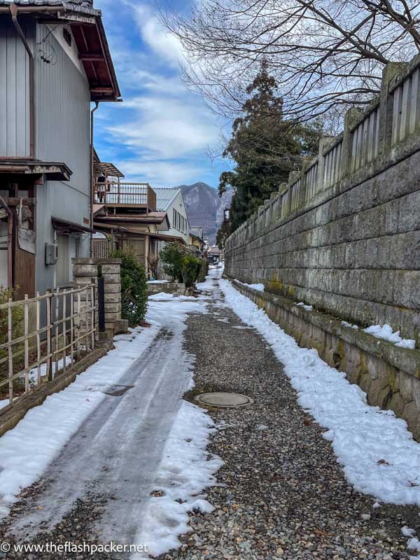 snow covered path between wall and wooden buildings in obuse japan