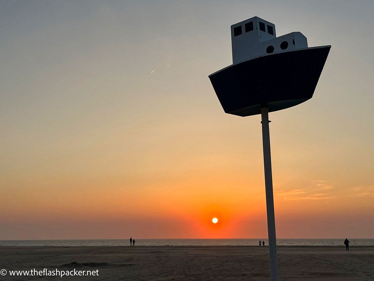 large installation of a boat on a pole on a beach at sunset