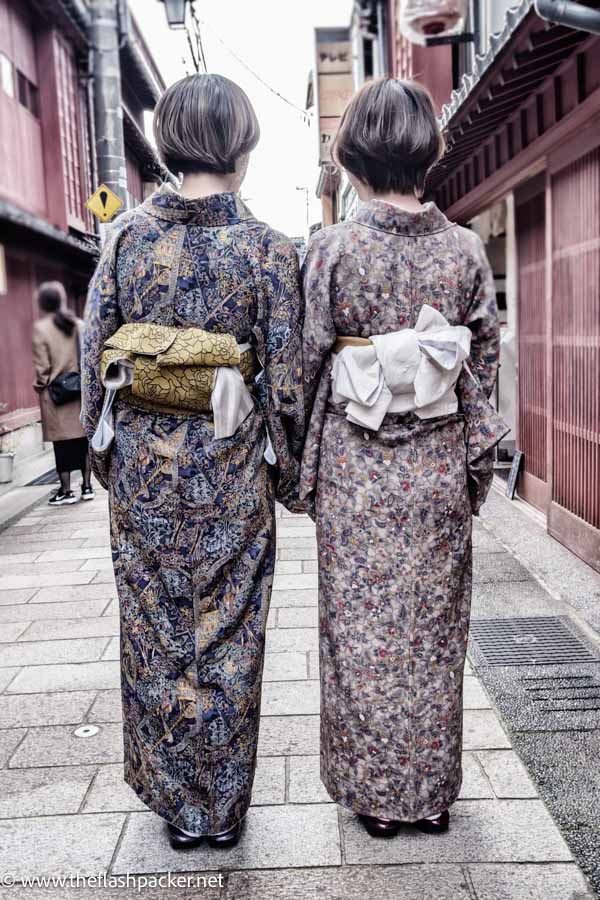 the back of two women dressed in kimonos walking along street