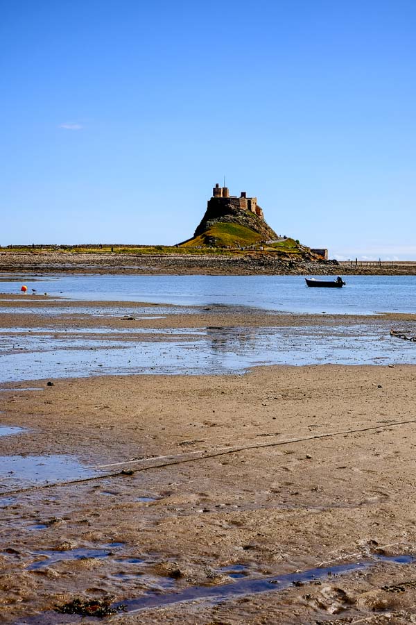 beach and shallow harbour with small boat in front of lindisfarne castle