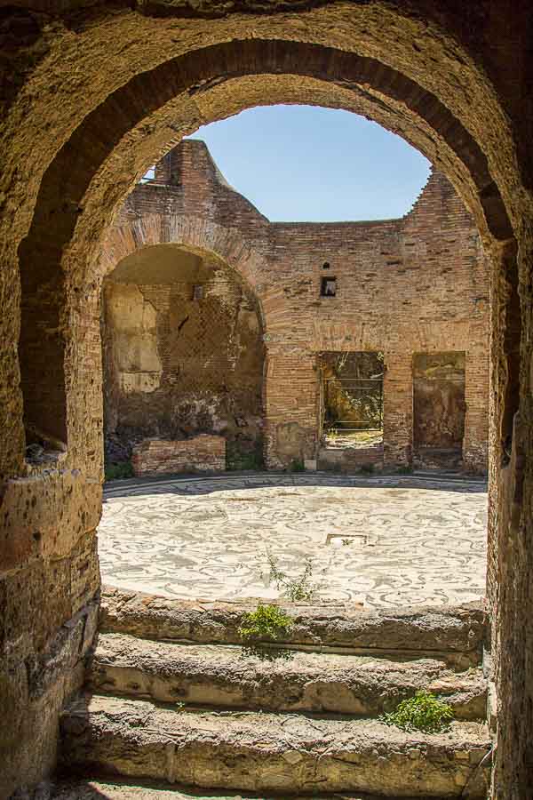 looking through stone arch to courtyard with mosaic floor at ostia antica rome