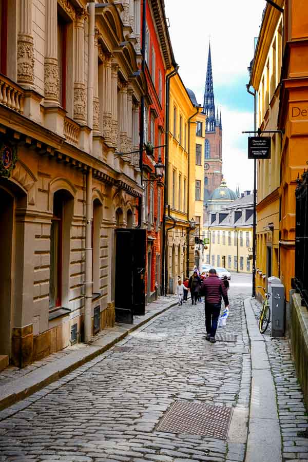 people walking along narrow street with church steeple in distance