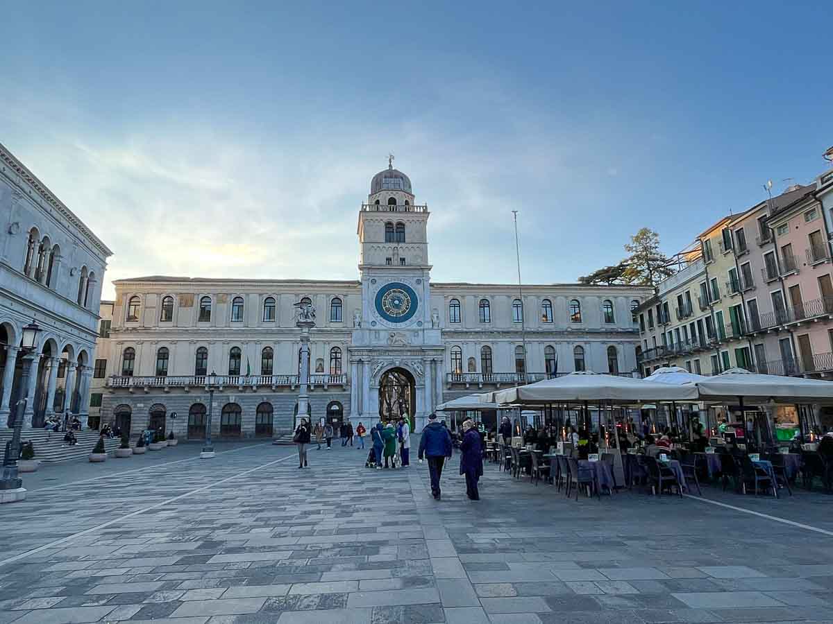 an elegant piazza in padua italy with a building with clock tower and people dining in terrace restaurants