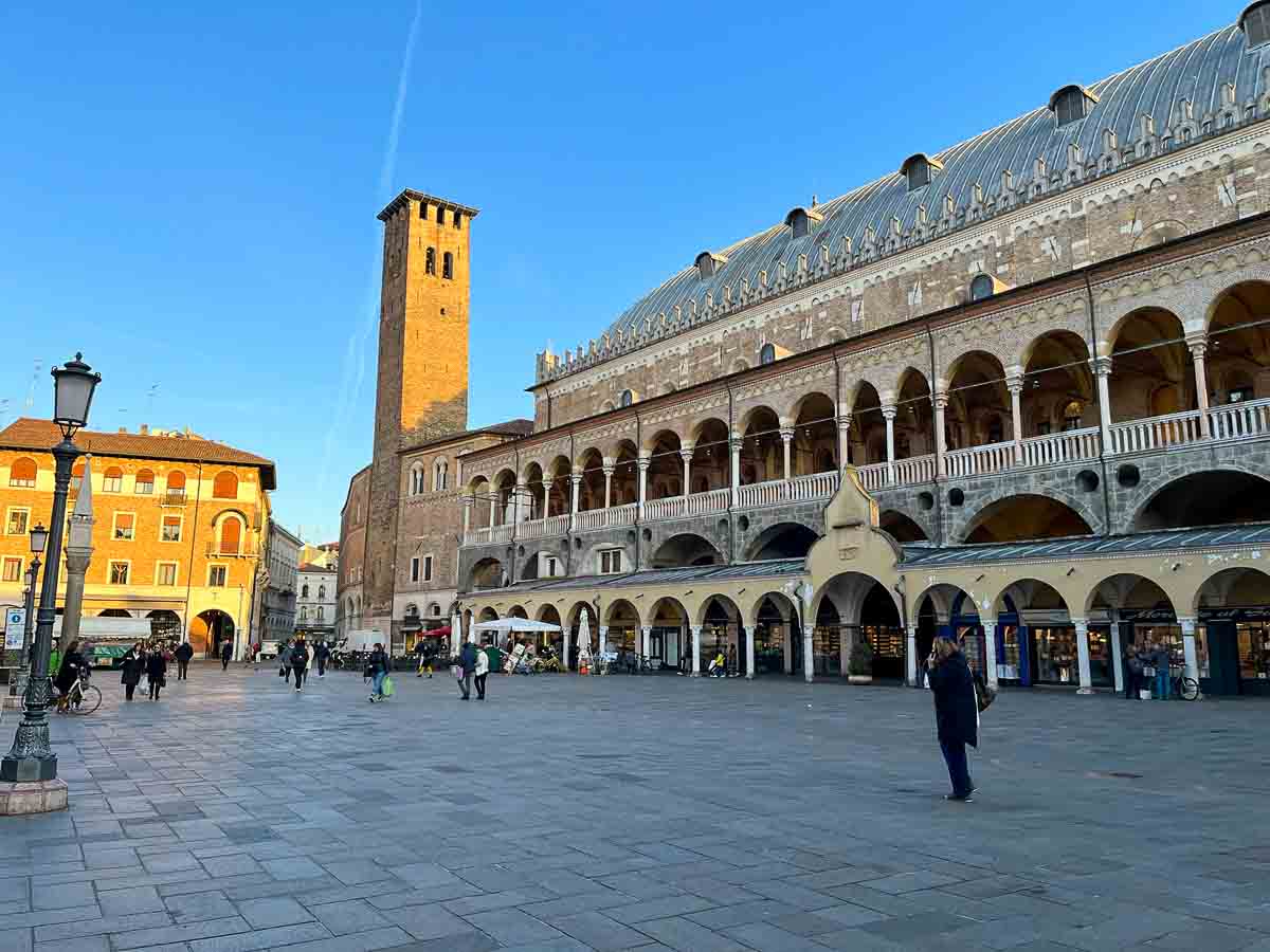 people walking across piazza in padua lined by an elegant porticoed palazzo