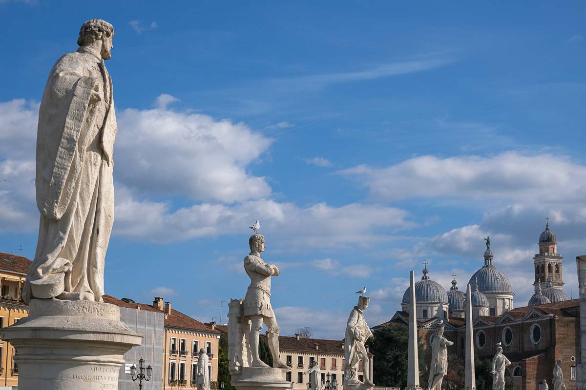 a line of large classical statues with the domes of a basilica in the background