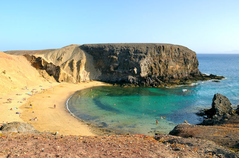 a sandy beach set in a cove with people bathing