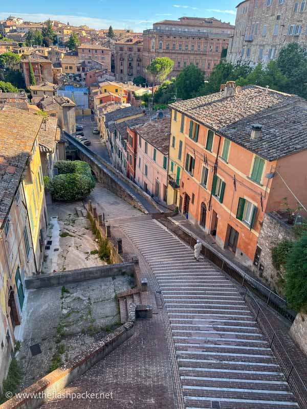 man walking down steps between pastel coloured buildings in perugia in umbria