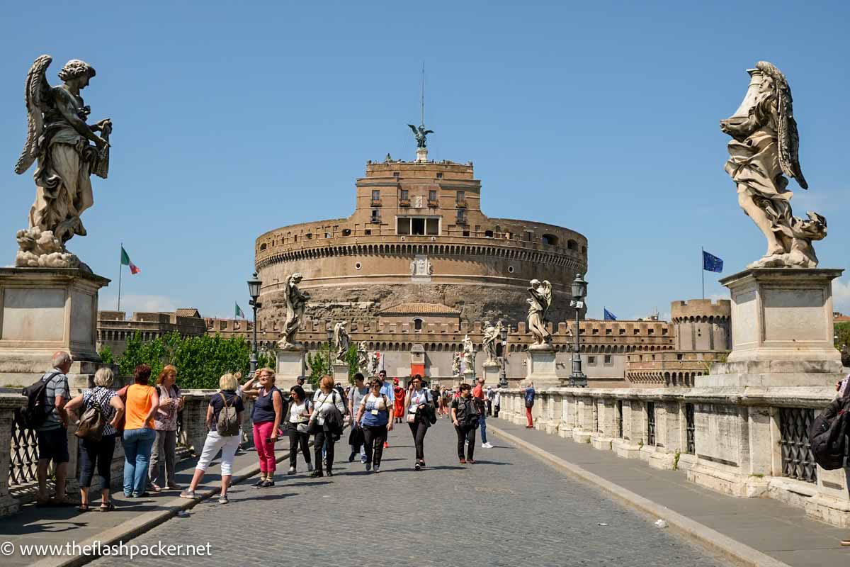 people walking across bridge to the large circular fort in rome of castel sant-angelo