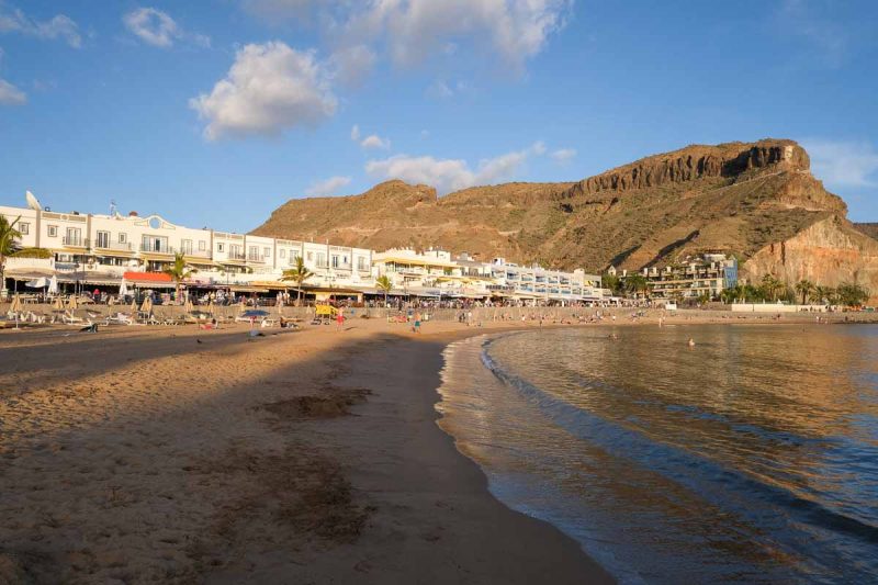 sandy beach lined with restaurants with cliff face in background