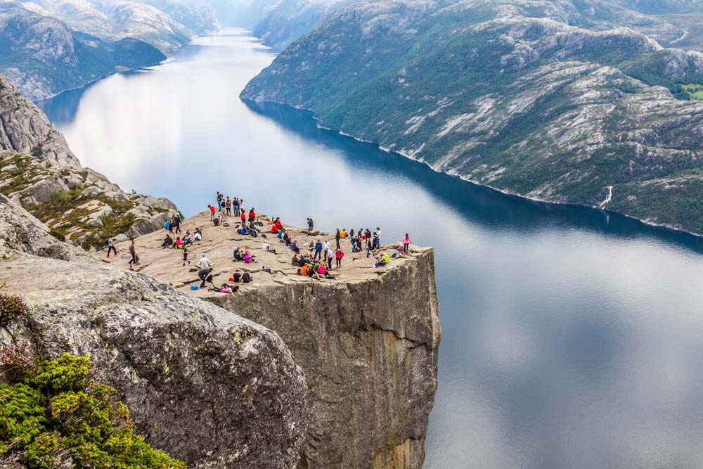 group of people on a rock shelf overlooking a deep fjord