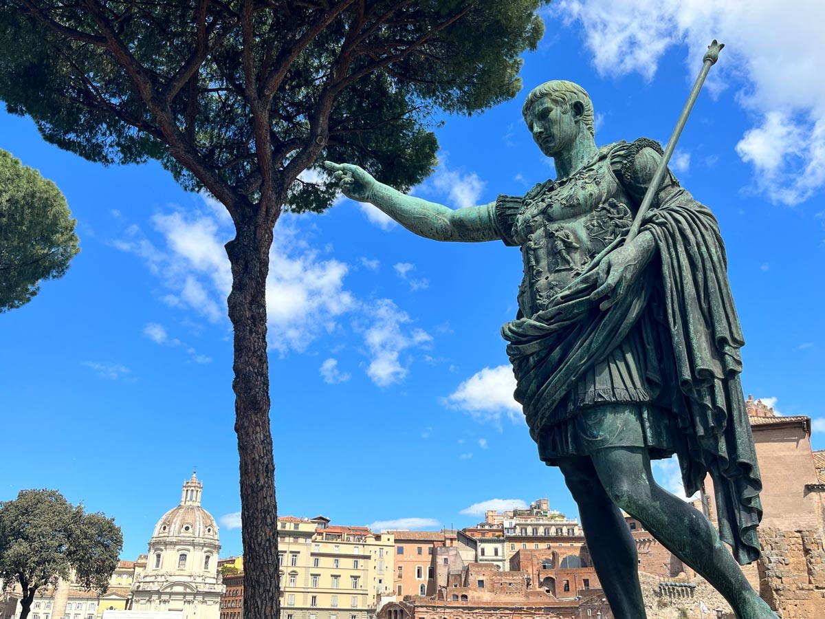 statue of roman soldier with outstretched hand in front of buildings in rome