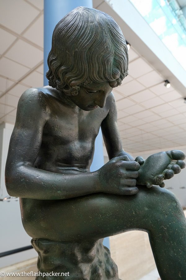 sculpture of boy looking at thorn in foot