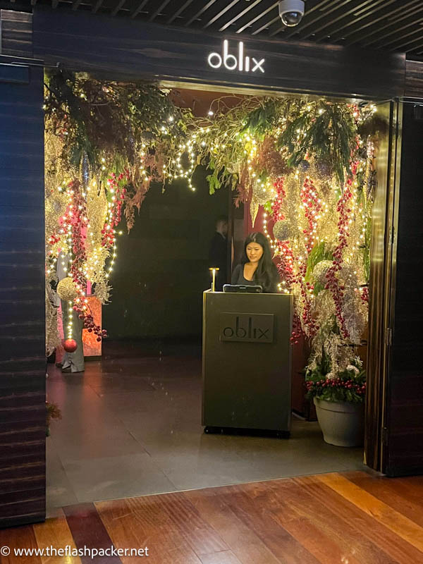 woman standing at entrance to oblix restaurant decorated with christmas lights