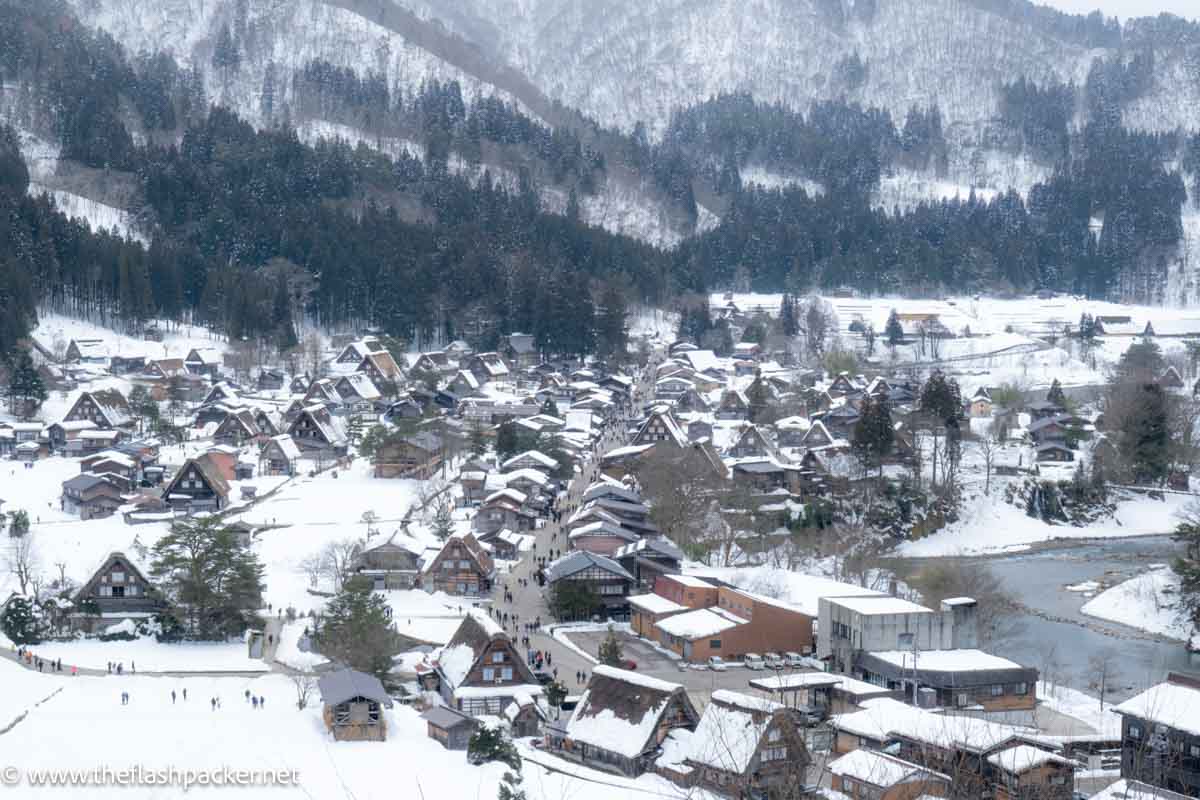 a snow covered valley filled with wooden framed a-shaped houses in shirakawago in japan