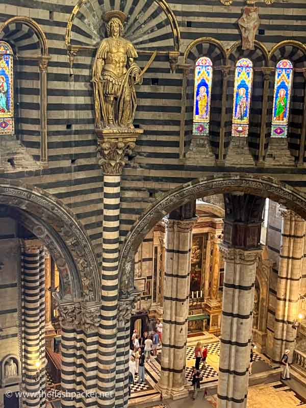 people walking between striped columns inside siena duomo