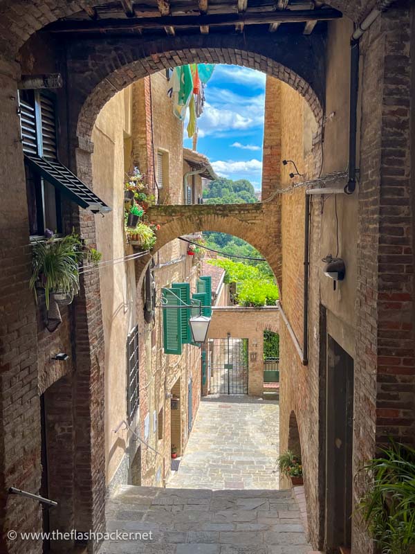 series of arches across a narrow street in siena with views over countryside