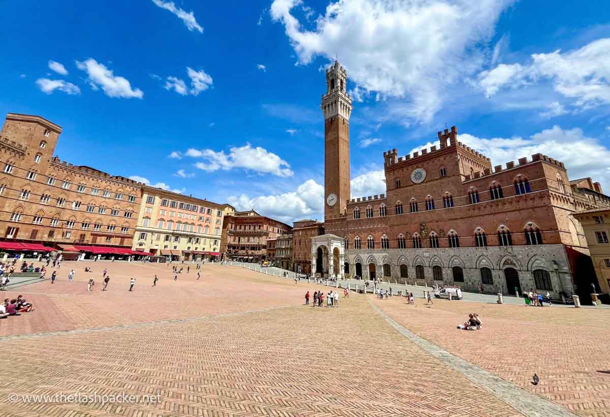 massive sloping piazza del campo in siena in tuscany bordered by red brick buildings including a large palazzo with clock tower