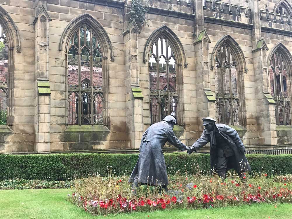 statue of two soldiers shaking hands in front of bombed out church