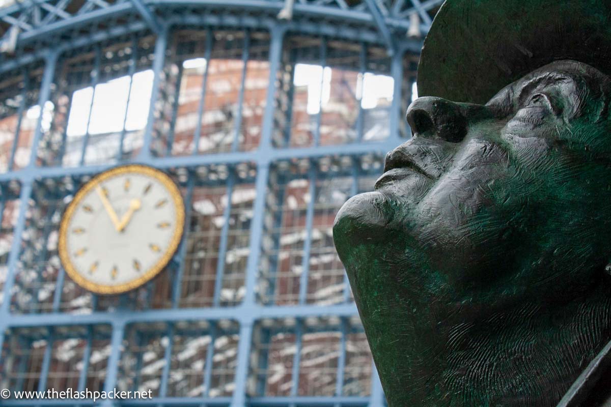 head of sir john betjeman statue in front of clock at st pancras station