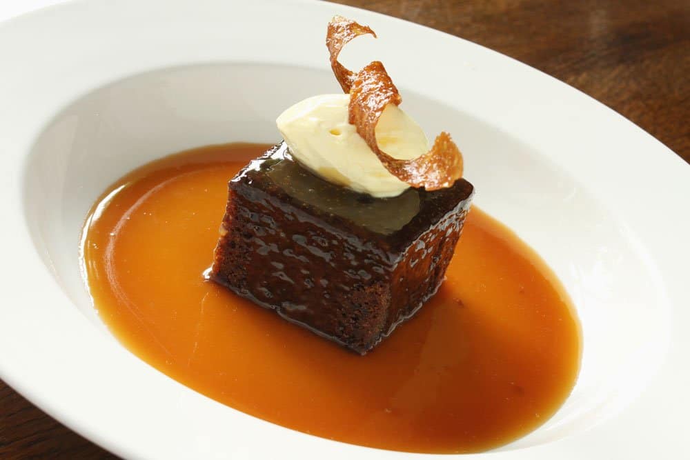 sticky toffee pudding in white bowl topped with ice cream