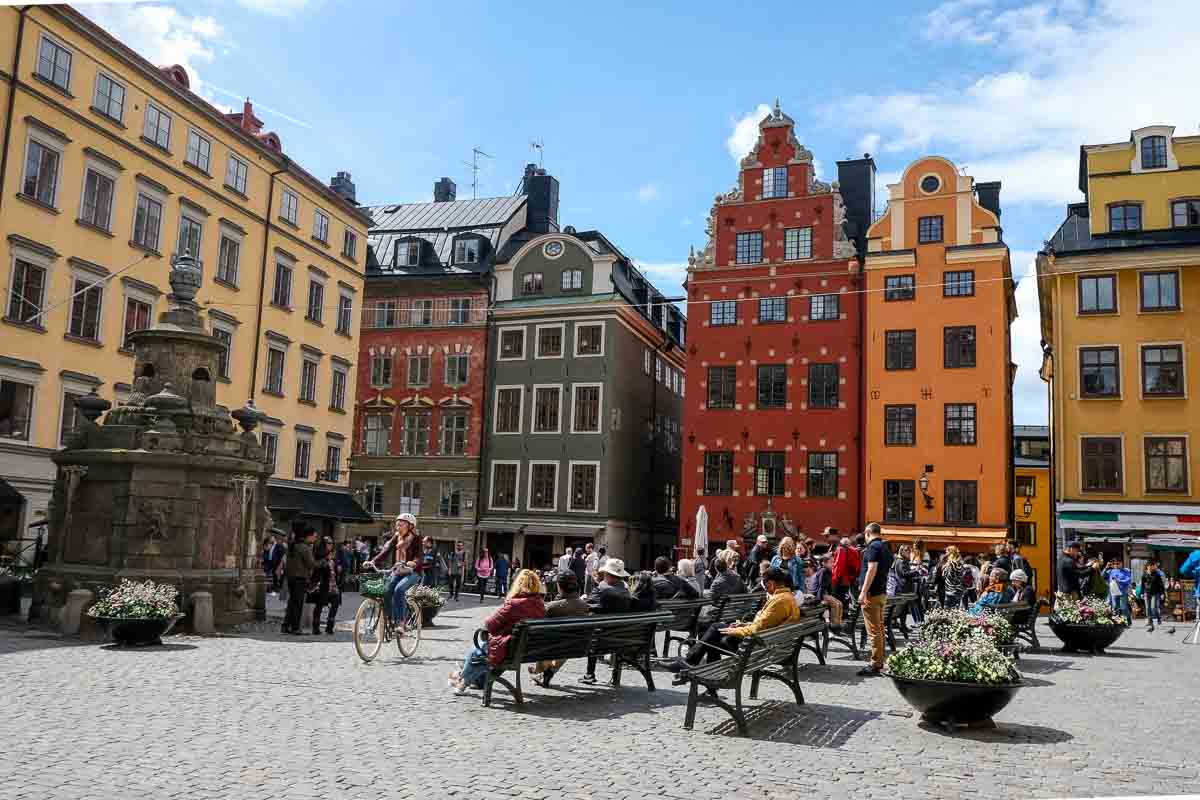 people sitting on benches in a cobblestoned square with gabled houses in stockholm