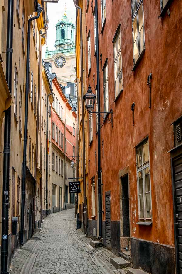 narrow cobblestone street lined with old ochre coloured buildings in stockholm old town and church bell tower