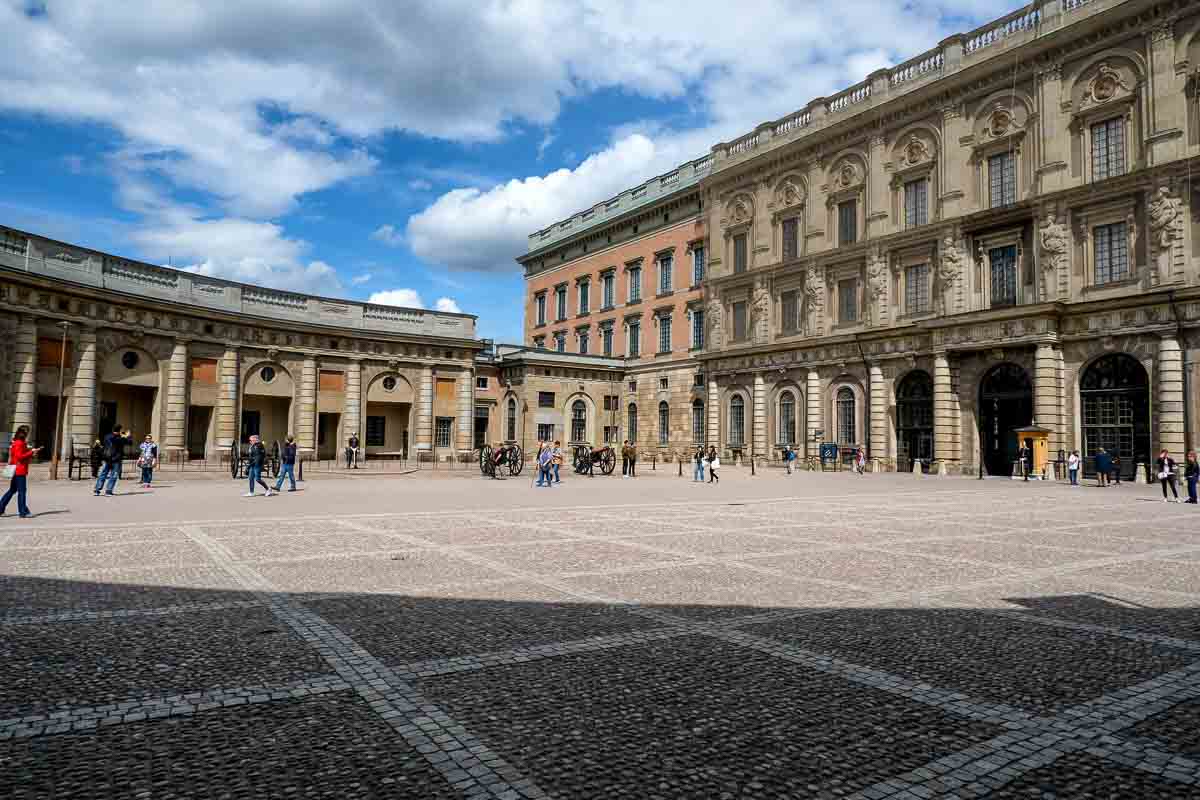 people walking across larke courtyard bordered by swedish royal palace buildings