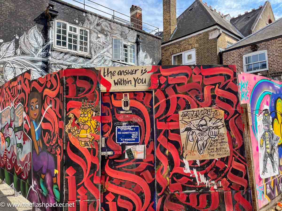 a wooden hoarding completely covered with street art and graffiti in brick lane london