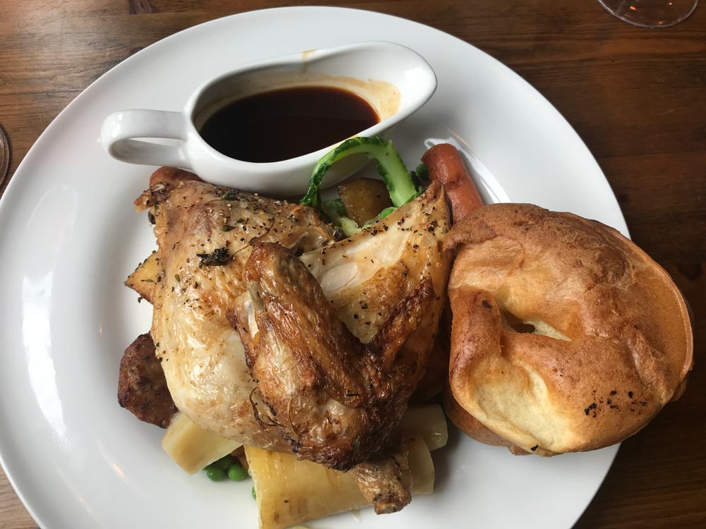 sunday roast dinner of chicken yorkshire pudding and vegetables on a white plate