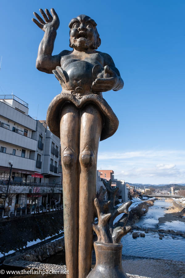 tall wooden statue of a grimacing man with his hand held up