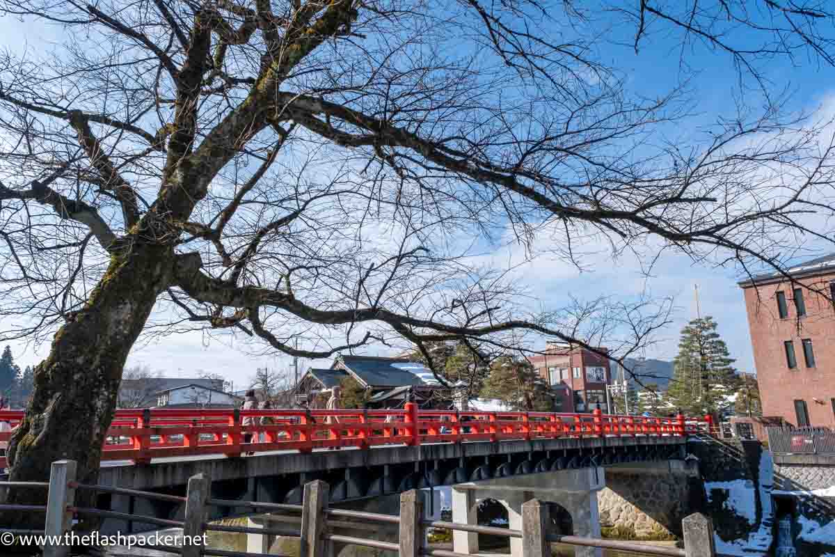 poeple walking across a pretty red bridge in takayama japan