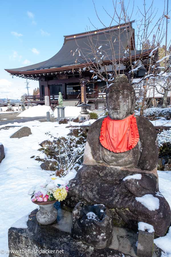 stone statue in front of a buddhist temple in the snow