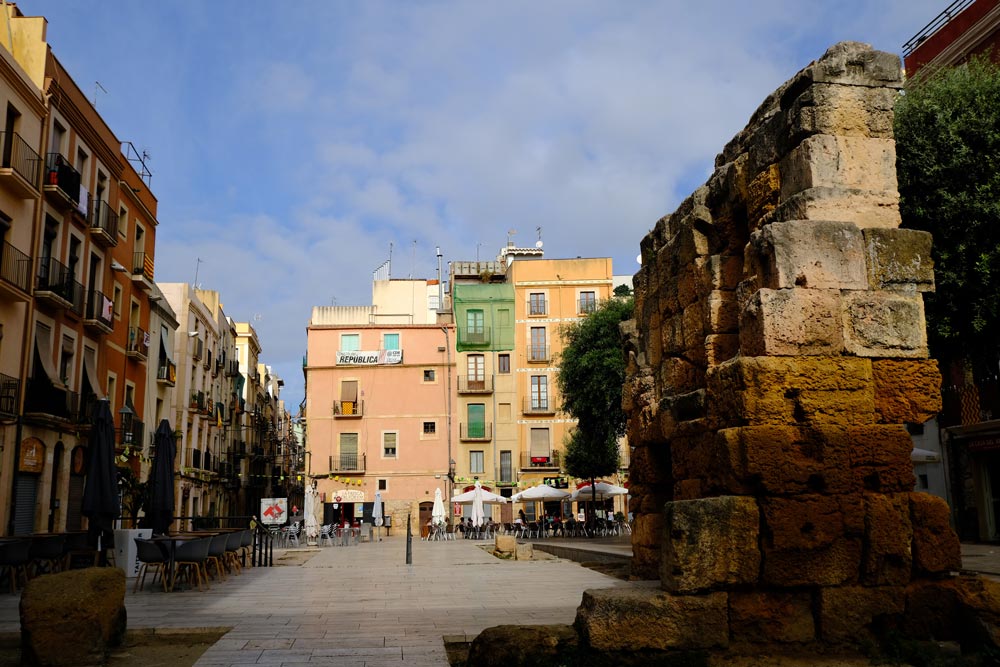 square in spanish city with ochre coloured buildings and roman ruins