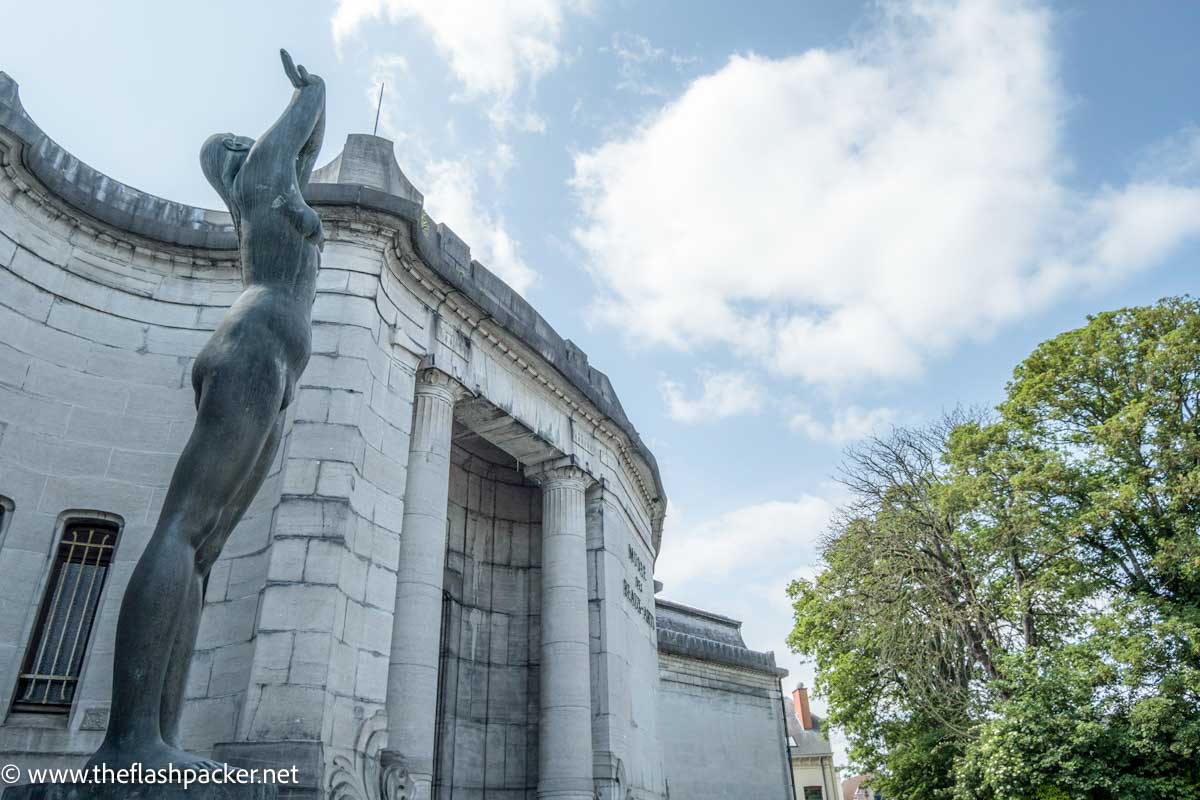 statues of naked woman with arms stretched over head in front of a grey art nouveau building